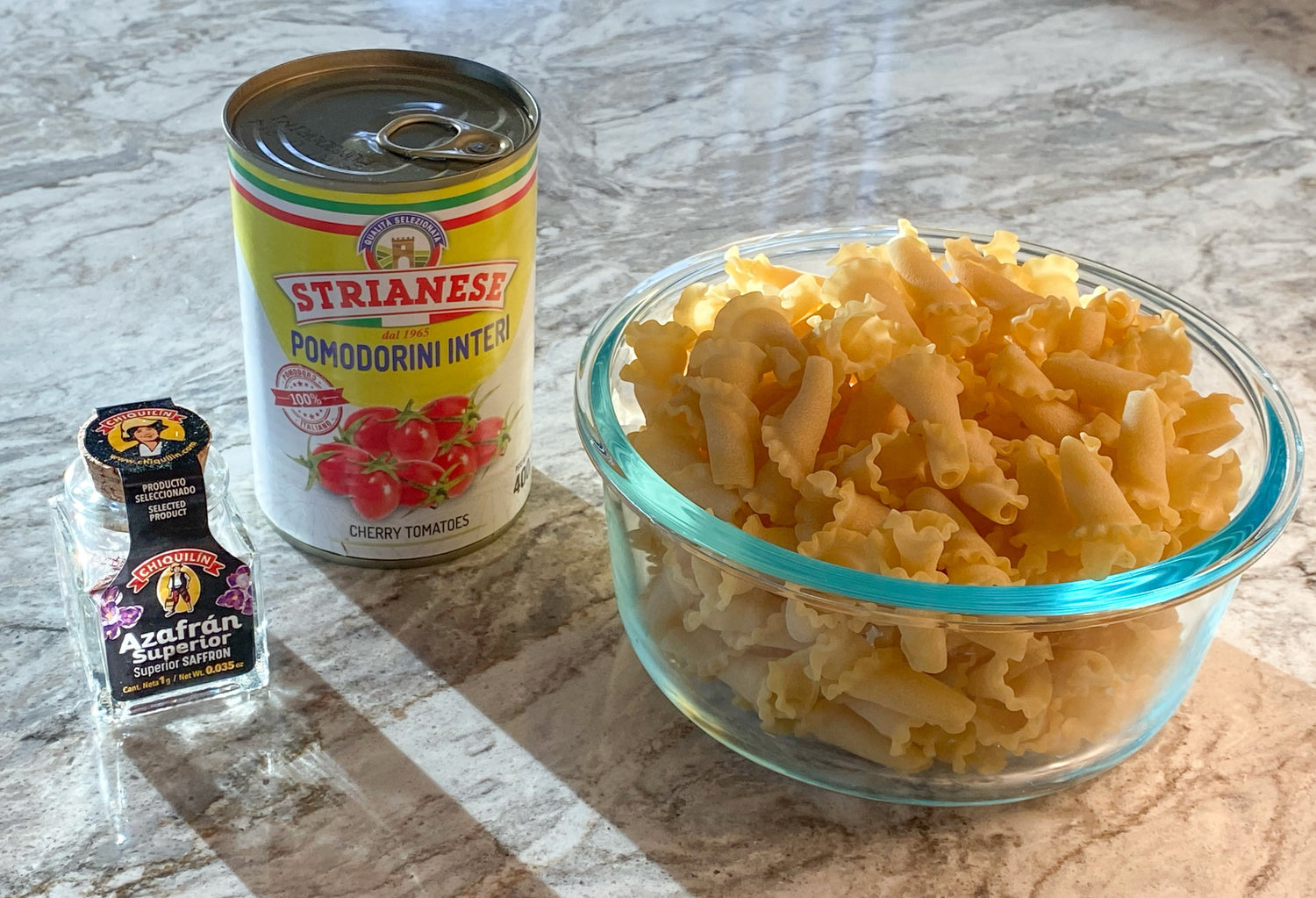 jar of saffron, can of Strianese brand imported cherry tomoatoes with a glass bowl filled with trombe pasta bowl of Trombe